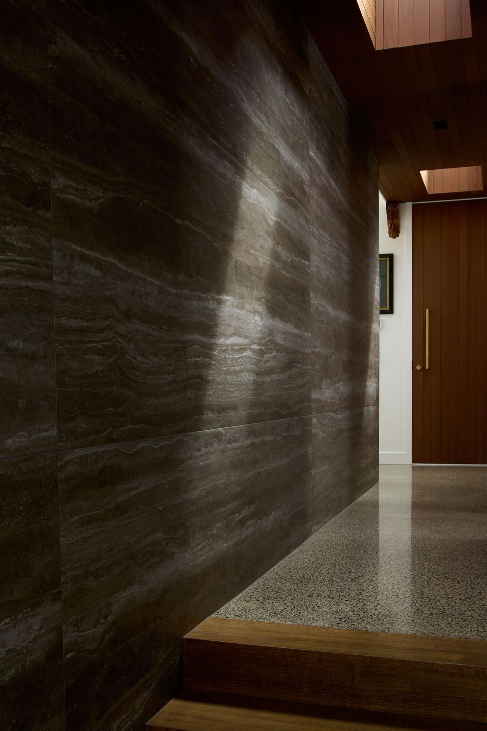 The hallway is defined by polished concrete floors, a cedar-lined skylight and textured stone wall tiles. Natural light draws visitors through the home while celebrating the richness of its material palette.