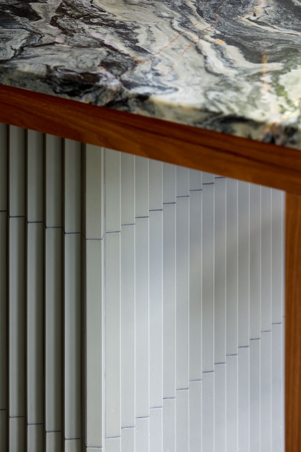 A close-up of the kitchen island highlights the richly veined granite benchtop, handcrafted tiled base and finely detailed walnut leg, showcasing the craftsmanship throughout the project.