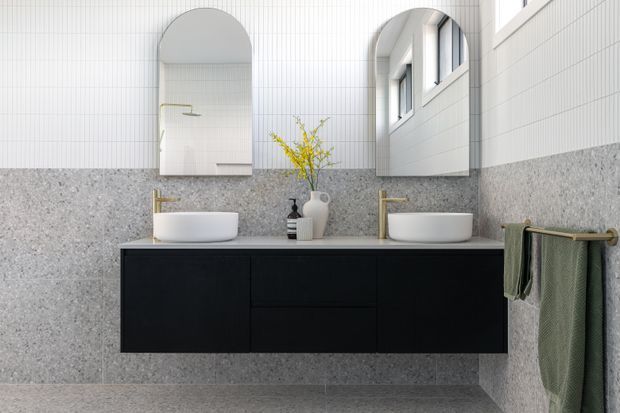 Bright contemporary bathroom featuring a double floating vanity with matte black cabinetry, white vessel basins, brushed brass taps and fixtures, grey terrazzo-style wall and floor surfaces, and white vertical tile walls. Two arched mirrors and high windows add architectural character and natural light.