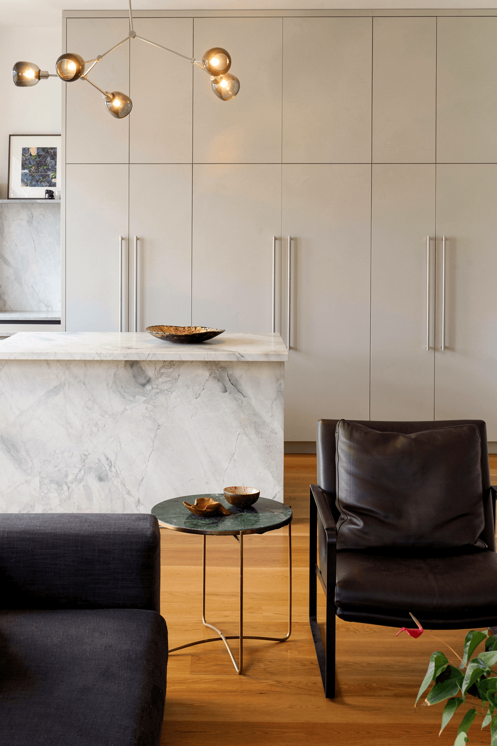 Viewed from the living room, the kitchen showcases its bespoke rear cabinetry, granite island and sculptural pendant lighting, creating a refined focal point within the open-plan interior.