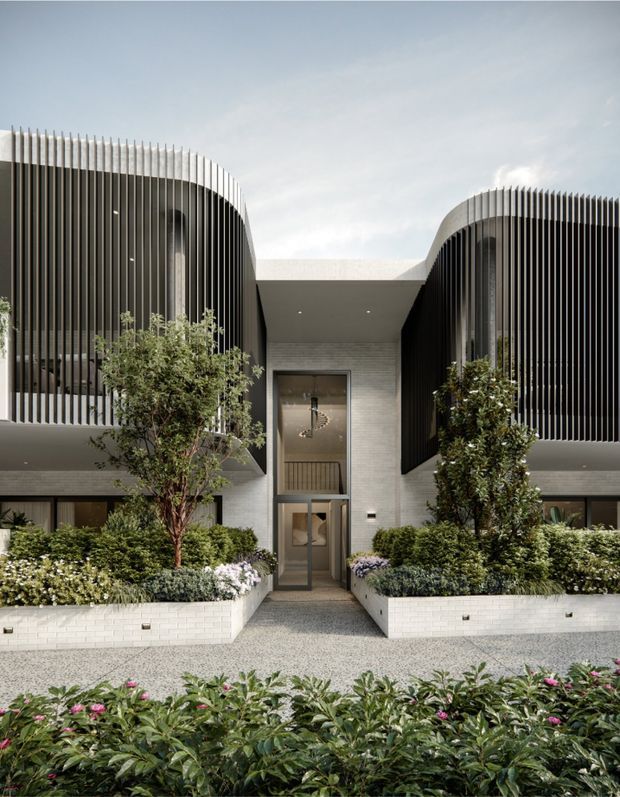 Front exterior view of a contemporary multi-unit residential building with symmetrical rounded wings wrapped in vertical dark screening fins. A recessed central entry is framed by light masonry, glazed doors, and a covered walkway, with raised white masonry planters and dense landscaped planting along the frontage.