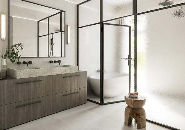A refined contemporary bathroom featuring a wide double vanity with grey wood-grain cabinetry, a pale textured stone benchtop, wall-mounted black tapware, and a large mirrored wall. Black-framed, fluted-glass shower and toilet enclosure create a strong grid-like architectural detail, while soft wall sconces and a sculptural timber stool add warmth.