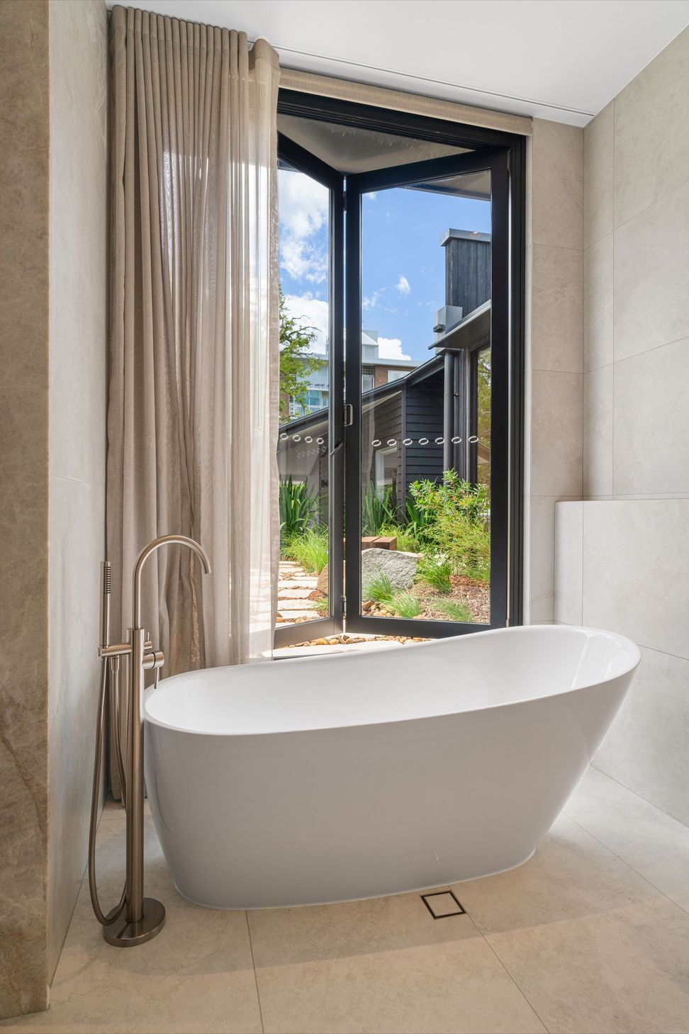 The main bathroom opens to the garden, pairing a sculptural bath with soft stone surfaces.