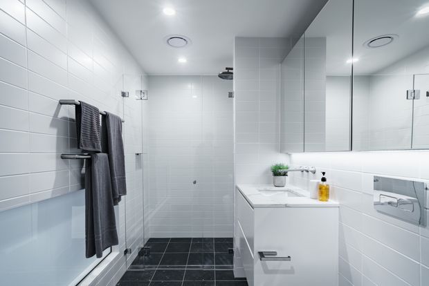 Bright contemporary bathroom with white tiled walls, a frameless glass walk-in shower, wall-mounted white vanity, large mirrored cabinet, chrome fixtures, and dark tiled flooring. Grey towels and a small plant add restrained contrast to the clean, minimalist fit-out.