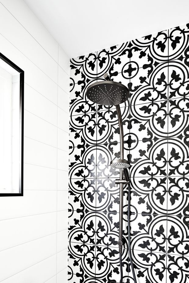 Close-up view of a contemporary shower enclosure featuring a black rain shower and handheld shower set against a striking black-and-white patterned tiled feature wall. Adjacent walls are clad in large-format white tiles with black-framed glazing or a mirror at the left edge.