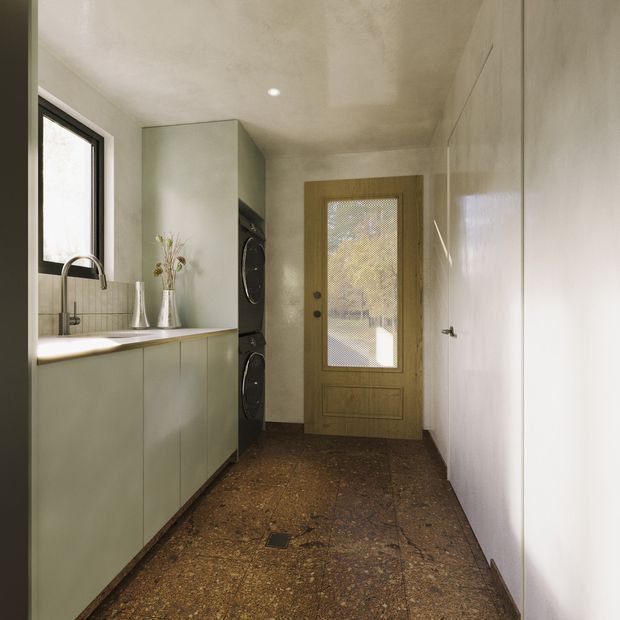 A narrow, contemporary laundry room with pale green built-in cabinetry, a white benchtop and integrated sink beneath a black-framed window. A stacked black washer and dryer sit beside the cabinetry. The room has a warm mottled brown hard floor, plain light walls, a timber-framed glazed exterior door, and a full-height white storage cupboard along the right wall.