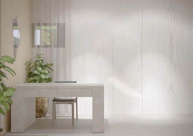 Bright, minimalist interior featuring a pale stone or concrete-style desk with integrated slab legs, a simple stool, indoor plants, sheer curtains, and vertically textured light wall and floor finishes. Soft daylight creates a calm, airy atmosphere.
