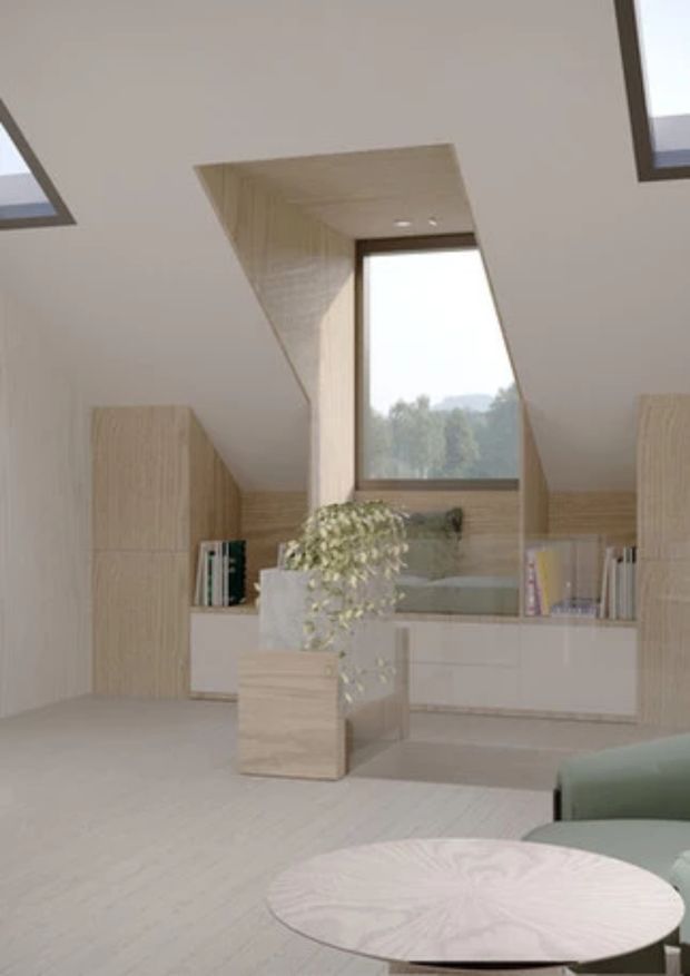 A bright, minimalist interior with pale timber flooring and built-in cabinetry surrounding a recessed window seat. Sloping ceilings feature skylights, while a central planter and round coffee table sit in front of a softly upholstered seating area. The palette is light and neutral with abundant natural light and integrated storage.