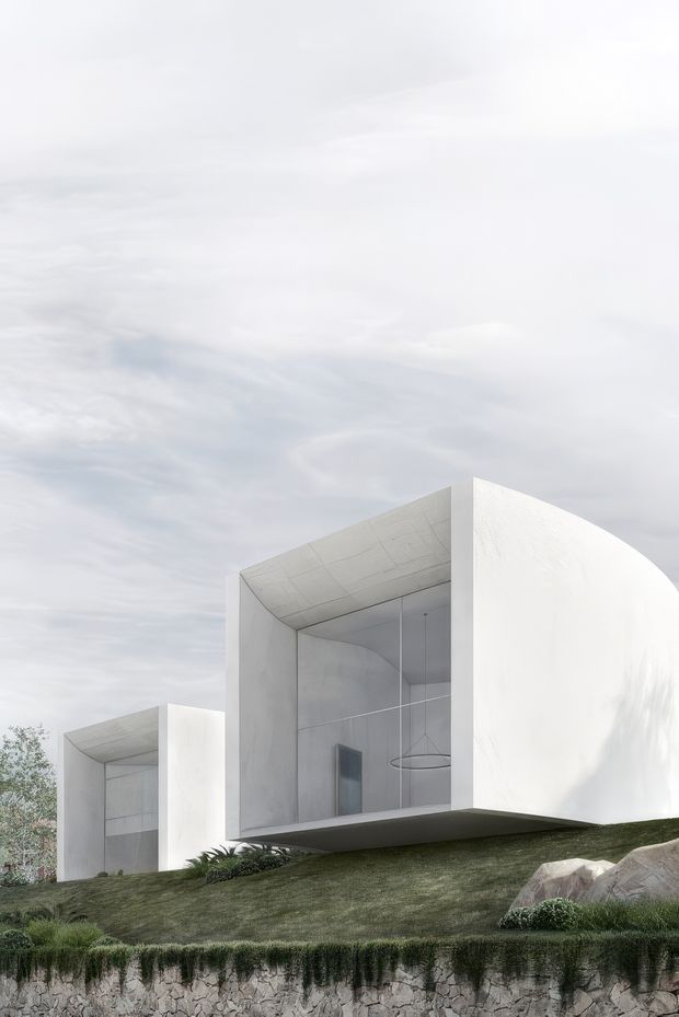 A minimalist white modern residence set into a sloping landscaped site. The sculptural building comprises curved and rectilinear volumes with large recessed glazed openings, smooth white exterior surfaces, and a projecting upper form. Low planting, lawn, rocks, and a rough stone retaining wall occupy the foreground beneath an overcast sky.