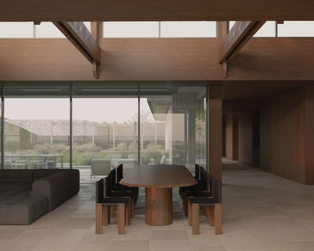 A refined open-plan dining and living area with a solid timber dining table and matching dark-framed timber chairs positioned beside a large glazed wall. A dark sectional sofa sits to the left, while a timber-lined circulation zone extends to the right. Exposed timber beams and a broad timber ceiling soffit create a strong structural rhythm, with views to a landscaped outdoor area through the glazing. The palette is warm, muted, and natural, with stone or porcelain-look floor tiling and extensive dark timber joinery.