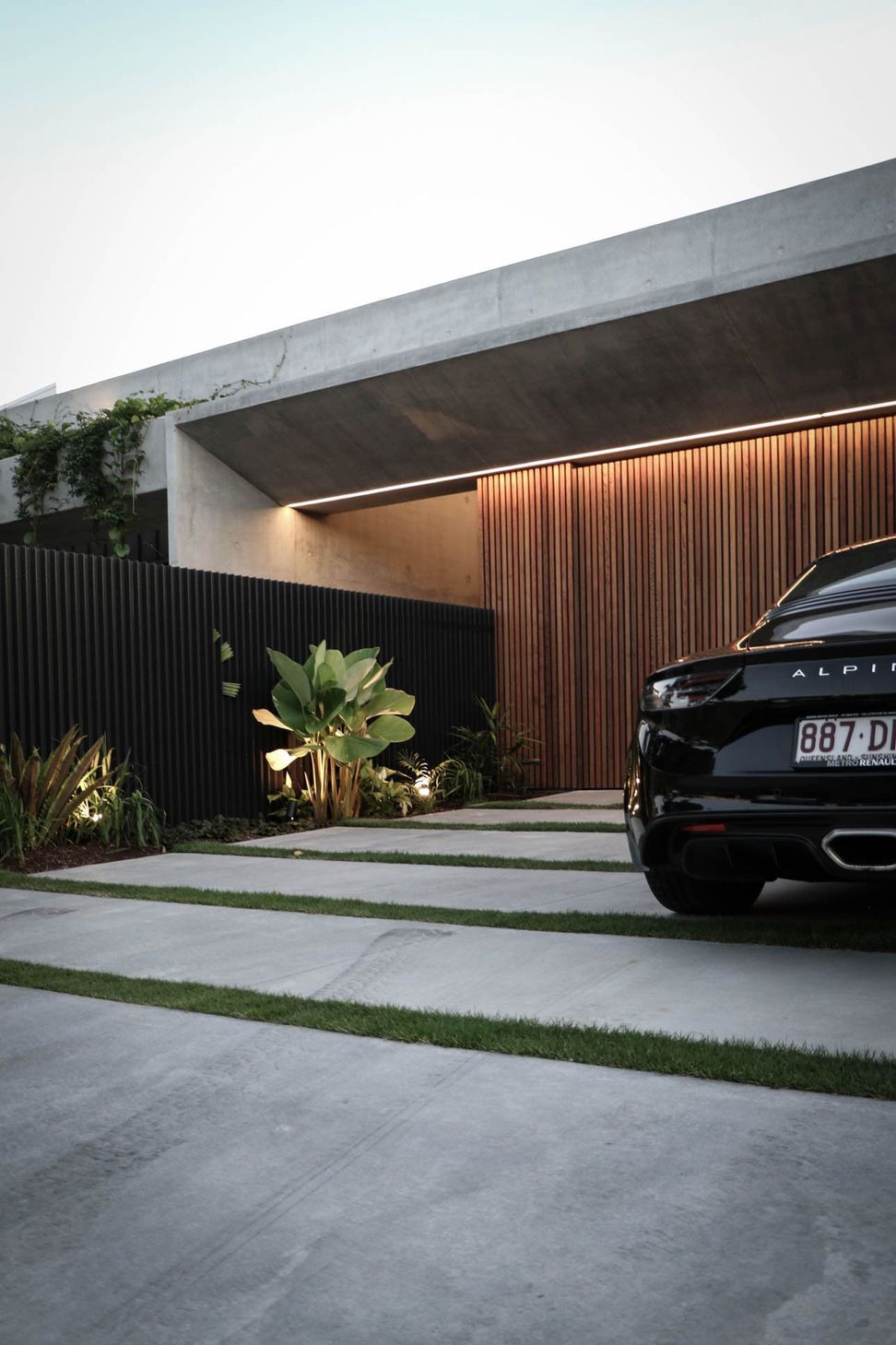 M Residence - Exterior. Driveway and timber clad garage lit at dusk.