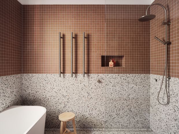 A contemporary bathroom featuring a freestanding white bathtub, walk-in shower with brushed metal fixtures, warm brown small-format tiled walls, and terrazzo-style speckled wall and floor surfaces. A recessed shower niche and vertical heated towel rails add functional detailing.