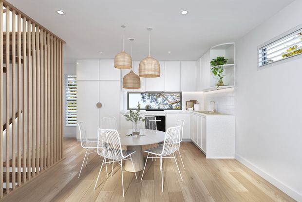 Bright, compact open-plan kitchen and dining area with white flat-panel cabinetry, a central dining table surrounded by white wire chairs, pale timber flooring, woven pendant lights, and a vertical timber slatted divider. High horizontal windows with louvres provide natural light, while open shelving adds greenery and simple styling.