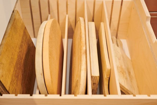 Close-up view inside a wooden storage drawer or cabinet containing vertically organized wooden boards, trays, and cutting boards. The image emphasizes natural timber construction and fitted dividers.