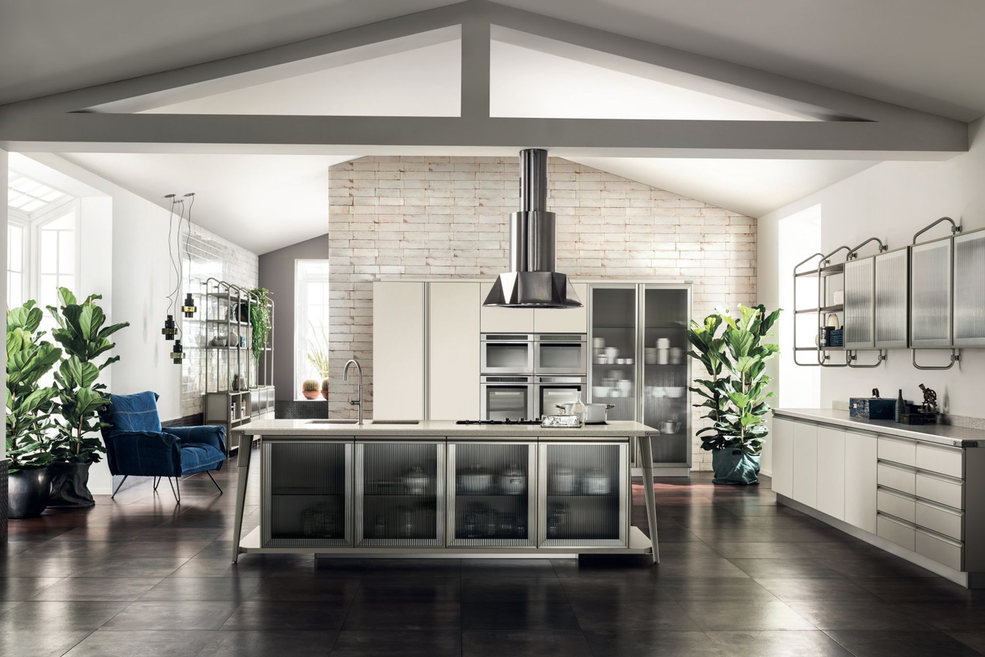 The large island appears to be suspended above the floor and the large supports, in Soft Steel finish metal, form a frame around the structures and the doors with Ribbed Glass. Both the washing area and the hob have been fitted flush with the matt finish Motley Quarz top.