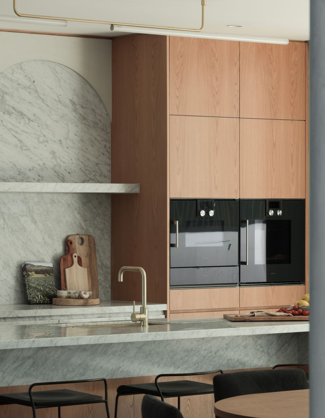 A central Alpine quartz stone wall anchors the design, complemented by a Carrara marble splashback and Gaggenau appliances. The adjoining wine bar framed by gentle curves creates a sense of refinement, balanced by travertine floors, white quartz pavers and marble enclaves. Details such as brushed brass tapware, green silk marble benchtops, and the Nood concrete pedestal bring character and intimacy, while textile lined robes and curved mirrors add a quiet elegance throughout.