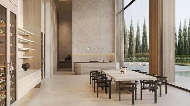 A refined open-plan kitchen and dining area with a long pale stone island, integrated light-wood cabinetry, open display shelving, and a large timber dining table with dark chairs. Full-height glazing opens the space to a landscaped outdoor area and pool, while a tall textured stone or plaster feature wall and concealed linear lighting add understated luxury.