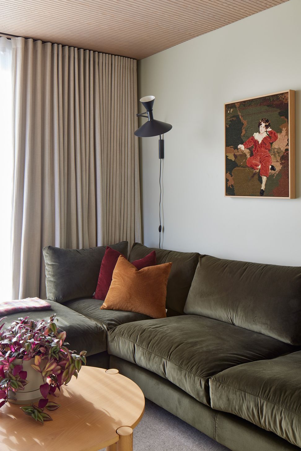 The separate lounge offers a quieter retreat within the home. A green velvet sofa, acoustic timber ceiling and sculptural wall light create a relaxed and intimate atmosphere.