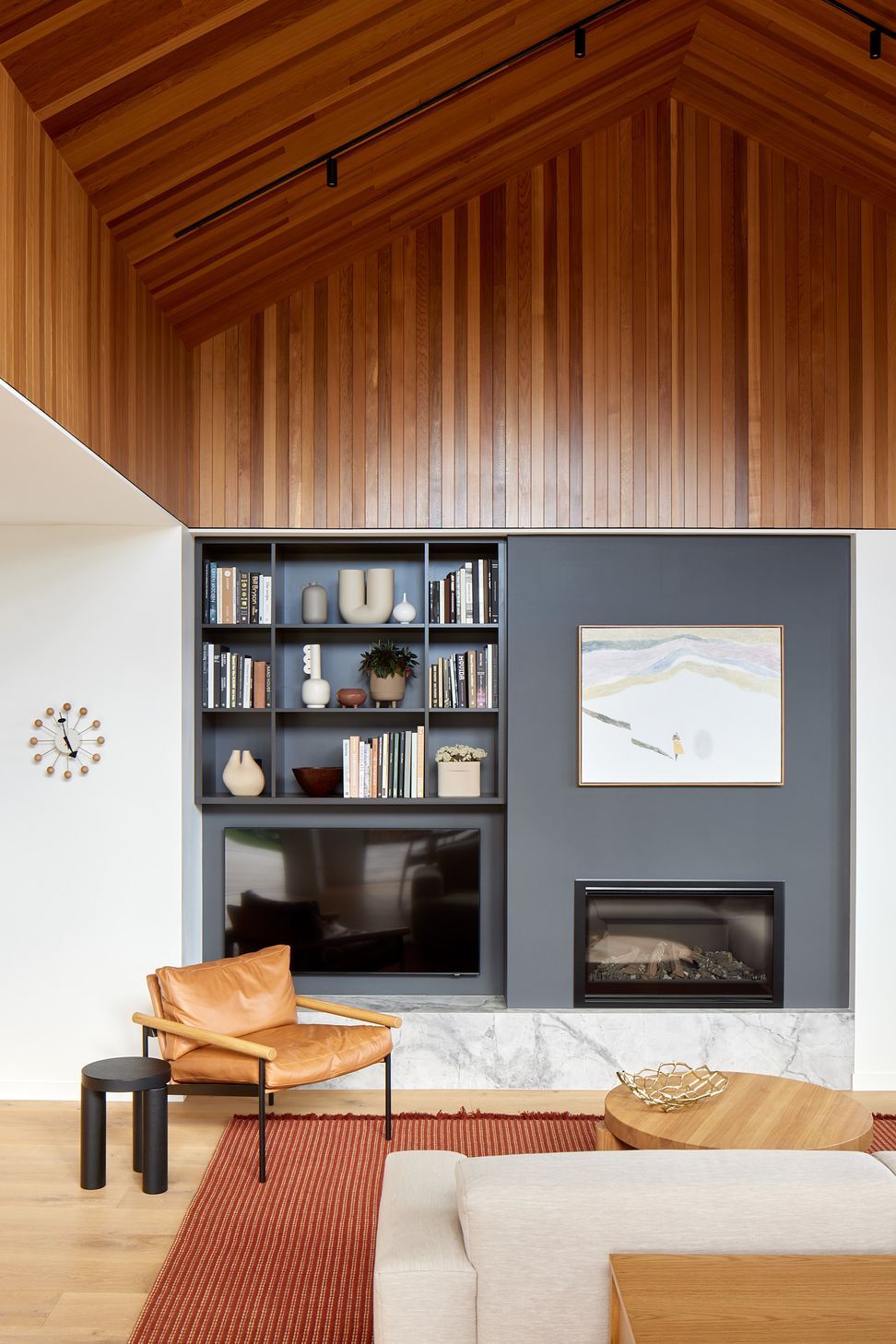 The living room is centred around bespoke grey cabinetry with an integrated fireplace. A cedar-lined ceiling introduces warmth and texture, creating a comfortable place for family life.