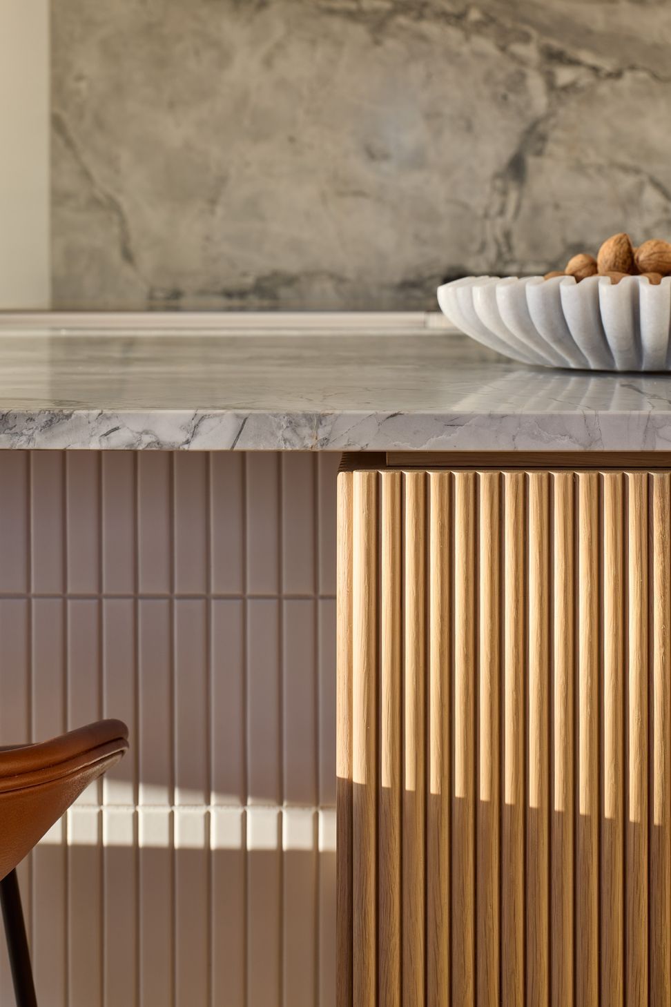A detailed view of the kitchen island reveals the Super White granite benchtop, rounded oak dowel detailing and handcrafted white tiled sides, celebrating the craftsmanship at the heart of the project.