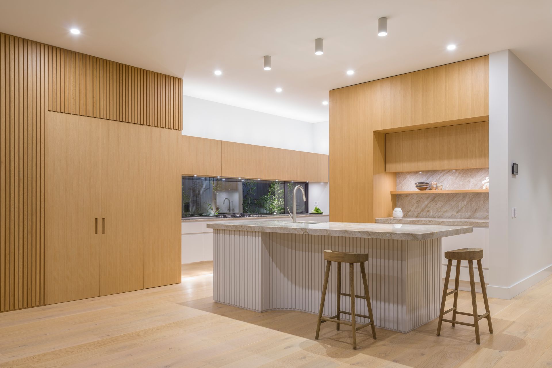 In true mid-century style, a dramatic 4.2 metre elongated window is configured as a key form. Long oak cupboards above and white drawers below repeat the same horizontal rhythm and proportions, emphasised by layering discreet LED lighting to each of the three levels.  Designed in 2019 before battened sheets became mainstream, each ‘pleat’ is carefully predetermined and dimensioned to read as evenly spaced even within the internal curvature. Like a perfectly hemmed garment, the battens just lightly skirt the floor.