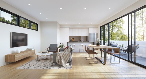Bright open-plan contemporary living and dining area with a compact white kitchen at the rear. The room features extensive black-framed floor-to-ceiling glazing, light timber flooring, a neutral sofa and lounge setting, a timber media console, and a long dining table beside the windows.