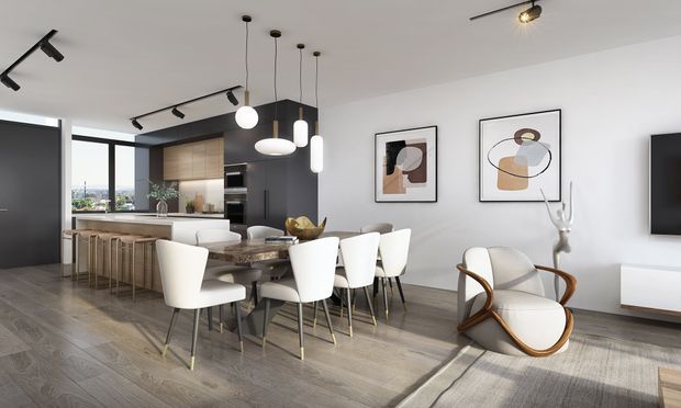 A contemporary open-plan apartment interior combining a kitchen, dining area and living zone. The space features a dark kitchen island with timber cabinetry, integrated appliances, a long dining table with upholstered chairs, sculptural pendant lighting, abstract wall art and a curved statement armchair. Large glazing brings in daylight and city views, while grey-toned timber flooring and white walls create a clean, refined atmosphere.