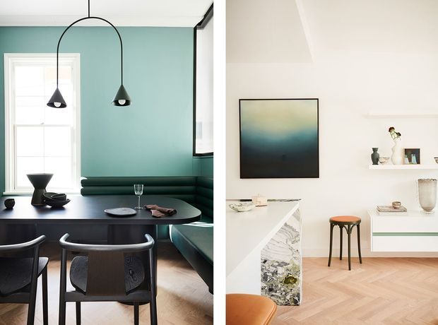 Split image showing two refined interiors. On the left is a compact dining and banquette area with a deep teal wall, dark built-in seating, a round dark table, sculptural pendant lights, and black-framed chairs. On the right is a bright minimalist kitchen or dining space with white walls and cabinetry, a marble-patterned island, pale timber herringbone flooring, open shelving, artwork, and a simple bar stool.