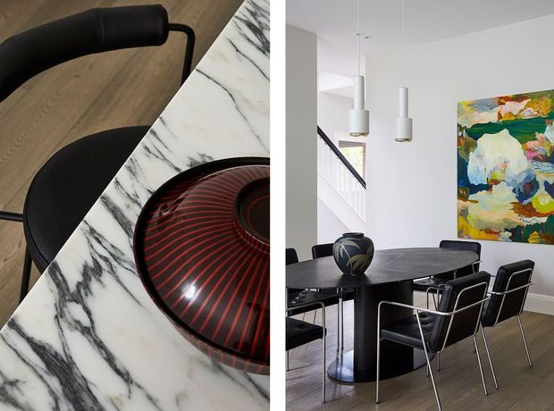 A split view of a contemporary dining area and close-up material detail. The dining room features a dark oval table with sculptural pedestal legs, black dining chairs, two cylindrical pendant lights, white walls, timber flooring, a staircase, and a large colourful abstract artwork. The close-up shows a veined white marble surface beside black seating and a decorative black-and-red bowl.