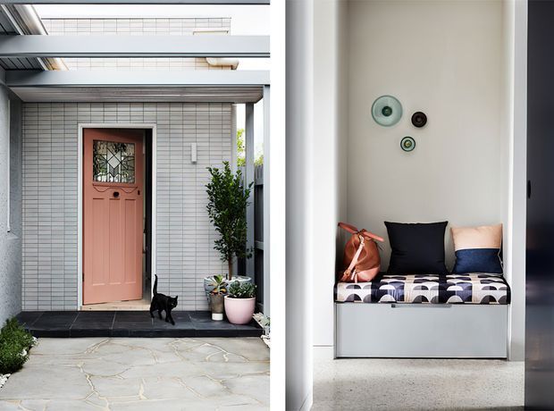 Split view of a contemporary home entry and a compact built-in window-seat nook. The exterior shows a pale tiled facade, projecting roof or canopy structure, dark threshold paving, and a muted coral entrance door with decorative glazing. The adjacent interior nook features a built-in upholstered bench with patterned cushion, dark and blush cushions, a small bag, and simple circular wall decor.