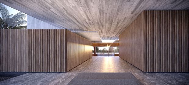 A dramatic contemporary interior entry or passageway with floor-to-ceiling vertical timber slat walls and a matching timber-lined ceiling. Dark stone-like flooring frames a lighter central timber walkway and rectangular rug, while daylight enters from an opening at the far end. Tropical foliage is visible beyond the glazing, adding an outdoor connection.
