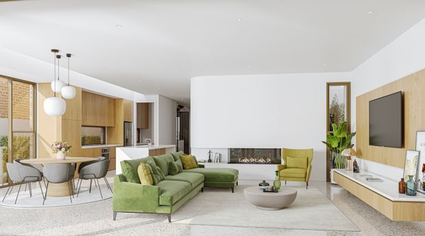 A bright, open-plan contemporary living and dining area with an integrated kitchen. The room features a pale terrazzo-like floor, white walls and ceiling, warm timber cabinetry and wall panelling, a green sectional sofa and matching accent chair, a linear fireplace, and a wall-mounted television. Large windows and glazed doors provide abundant natural light.