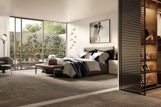 Contemporary bedroom with a large upholstered bed, layered neutral bedding, bedside storage, a low coffee table, and a lounge chair. Full-height glazed doors open visually to a planted courtyard, while a dark horizontal slatted divider screens a timber-lined walk-in wardrobe. The room has a restrained neutral palette, streamlined built-in elements, and abundant natural light.