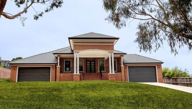 Front exterior view of a substantial brick residential house on a gently sloping lawn. The home has a symmetrical facade with a central covered entry porch supported by white columns, a tiled hipped roof, multi-pane windows, and attached double garages on both sides. Mature trees and fencing frame the property.