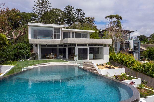 Exterior view of a contemporary multi-level residence set in a leafy suburban landscape, with extensive glazing, projecting concrete terraces, a landscaped garden and a large curving swimming pool in the foreground.