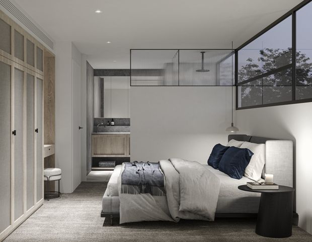 A refined contemporary bedroom with a large upholstered bed, layered white bedding, and navy cushions. Full-height built-in wardrobe doors line the left wall, while a compact ensuite bathroom is visible at the rear. Black-framed internal glazing and a mezzanine-like upper void add architectural interest, with neutral grey carpeting, white walls, and dark timber or stone accents creating a calm, monochromatic scheme.