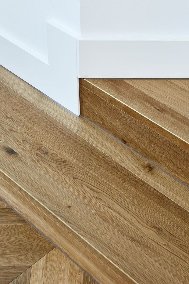 Close-up detail of a timber staircase with warm natural wood treads and risers, visible grain and fine contrasting inlay lines. White painted walls and a crisp white stair stringer create a clean, minimalist architectural finish.