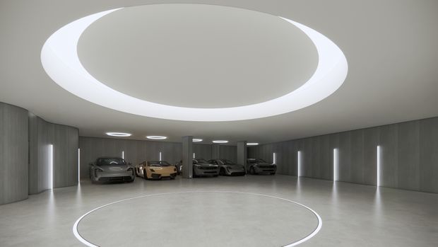 A large, futuristic indoor vehicle showroom or private car gallery with several cars displayed along the perimeter. The space has smooth grey architectural surfaces, integrated vertical strip lighting, a polished light-grey floor, and a dramatic circular recessed ceiling feature with luminous ring lighting. A matching circular floor inlay defines the central display area.