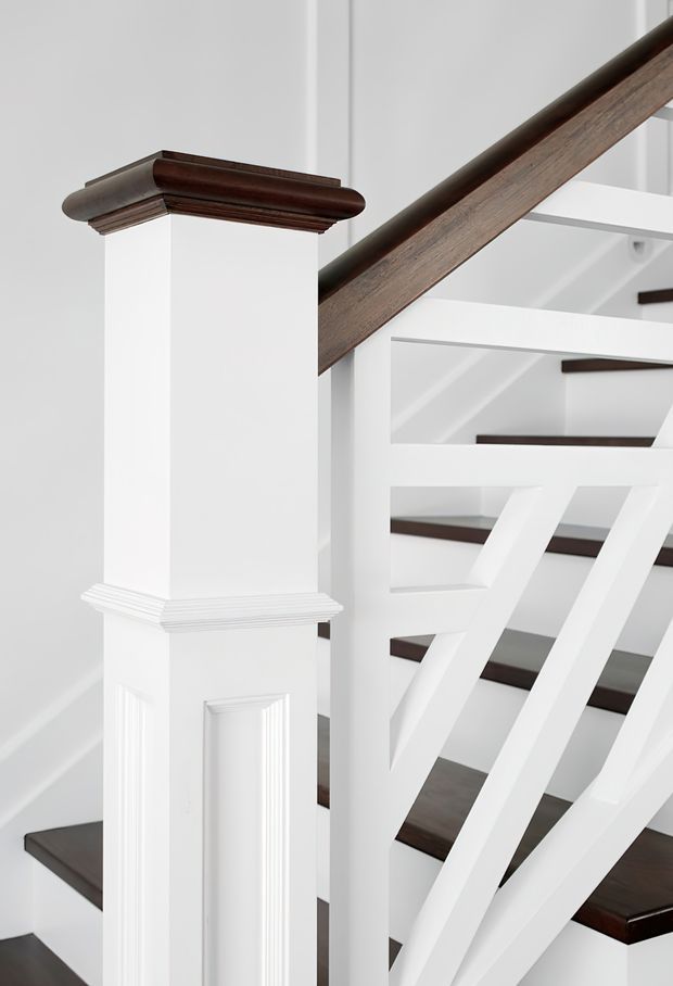 Close-up architectural detail of a traditional-style interior staircase. The stair has dark stained timber treads and handrail, white painted balustrades and risers, and a substantial white newel post with decorative moulded trim and raised panel detailing.