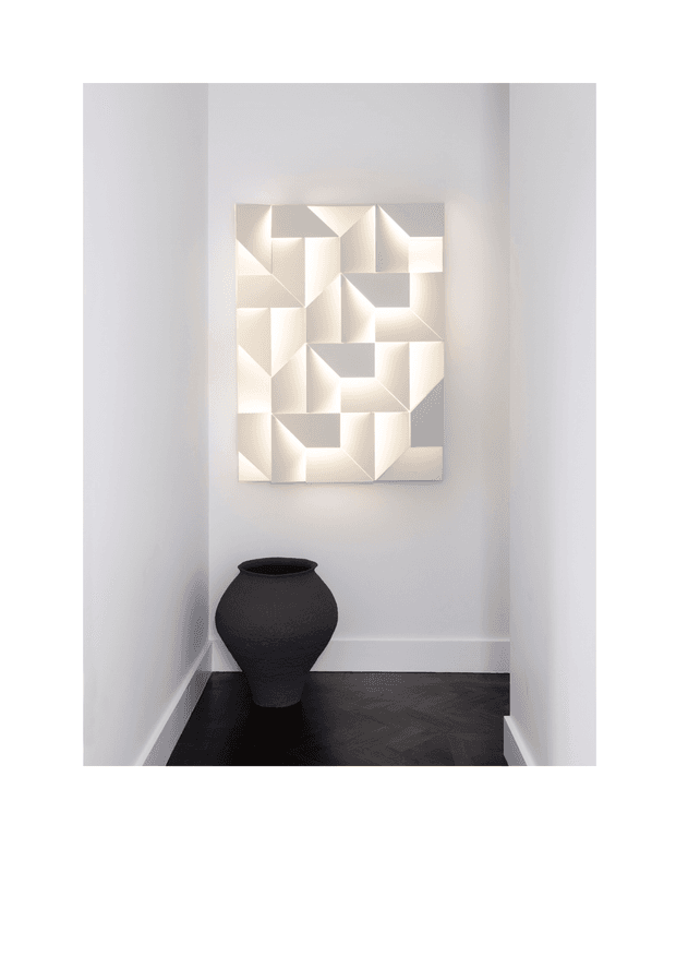 A minimalist hallway or entry niche with pale grey walls, white skirting boards, and a dark herringbone timber floor. A large geometric white sculptural artwork is mounted on the end wall above a matte black rounded ceramic vessel, creating a restrained, high-contrast composition.