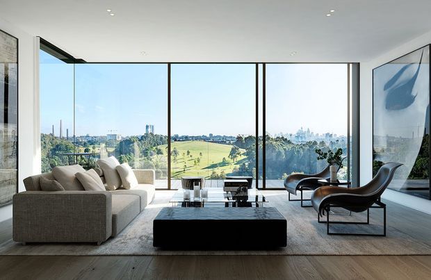 A bright, spacious contemporary living room with floor-to-ceiling glazing overlooking a green parkland landscape and distant city skyline. The room features a large neutral sectional sofa, sculptural lounge chairs, a low black rectangular coffee table, minimalist artwork, recessed ceiling lights, and wide timber flooring.