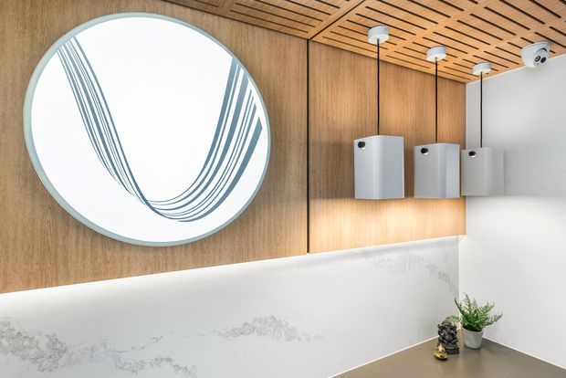 Close-up view of a contemporary bathroom vanity area featuring a large round mirror, warm timber wall and slatted ceiling, white marble-look wall surfaces, and three suspended rectangular pendant lights. Small potted plants sit on the vanity, adding a natural accent.