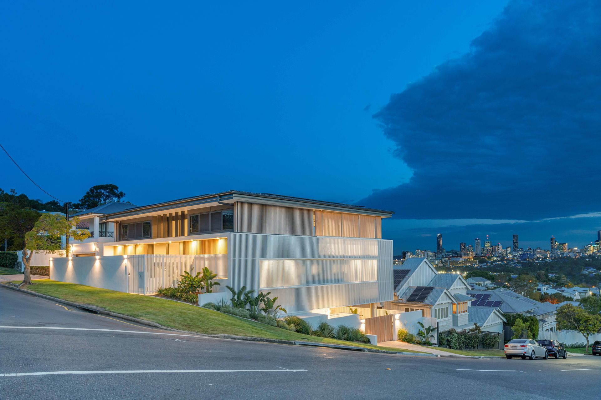 At dusk, the home's corrugated batten cladding glows against the city skyline beyond.