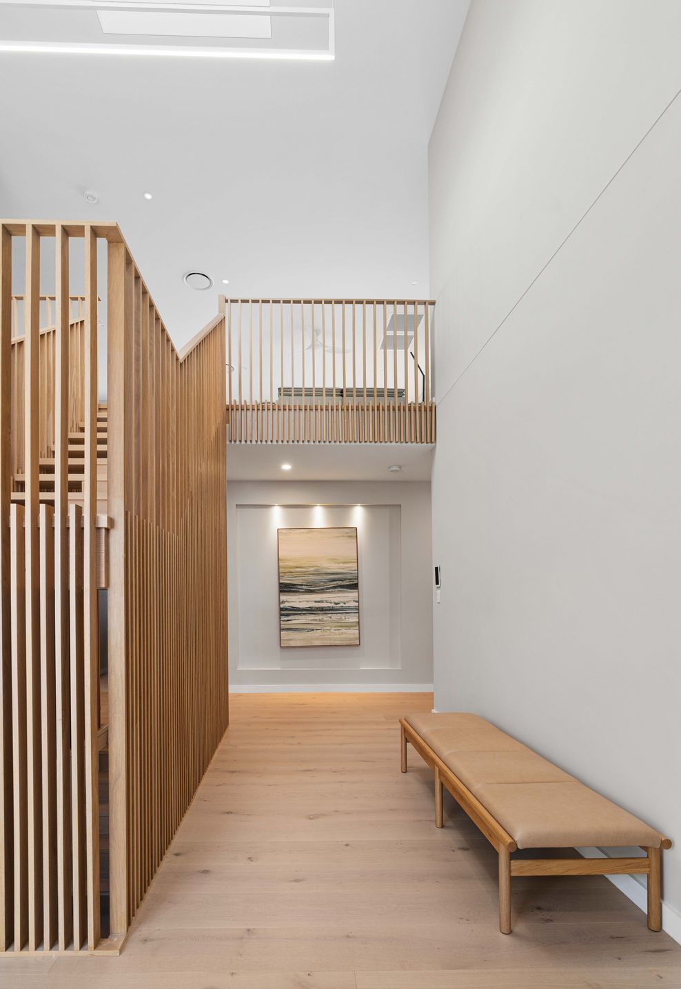 Timber slats wrap the stairwell void, light falling through the skylight above.