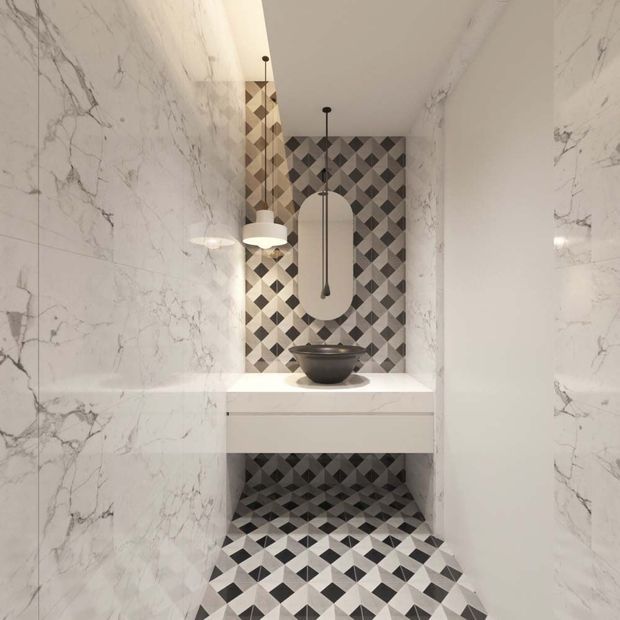 A narrow, refined bathroom or powder room clad in white marble-look wall surfaces, with a striking geometric black, grey and white tiled floor and matching feature backsplash. A floating white vanity supports a dark vessel basin, while a tall oval mirror and layered pendant lights create a luxurious focal point.