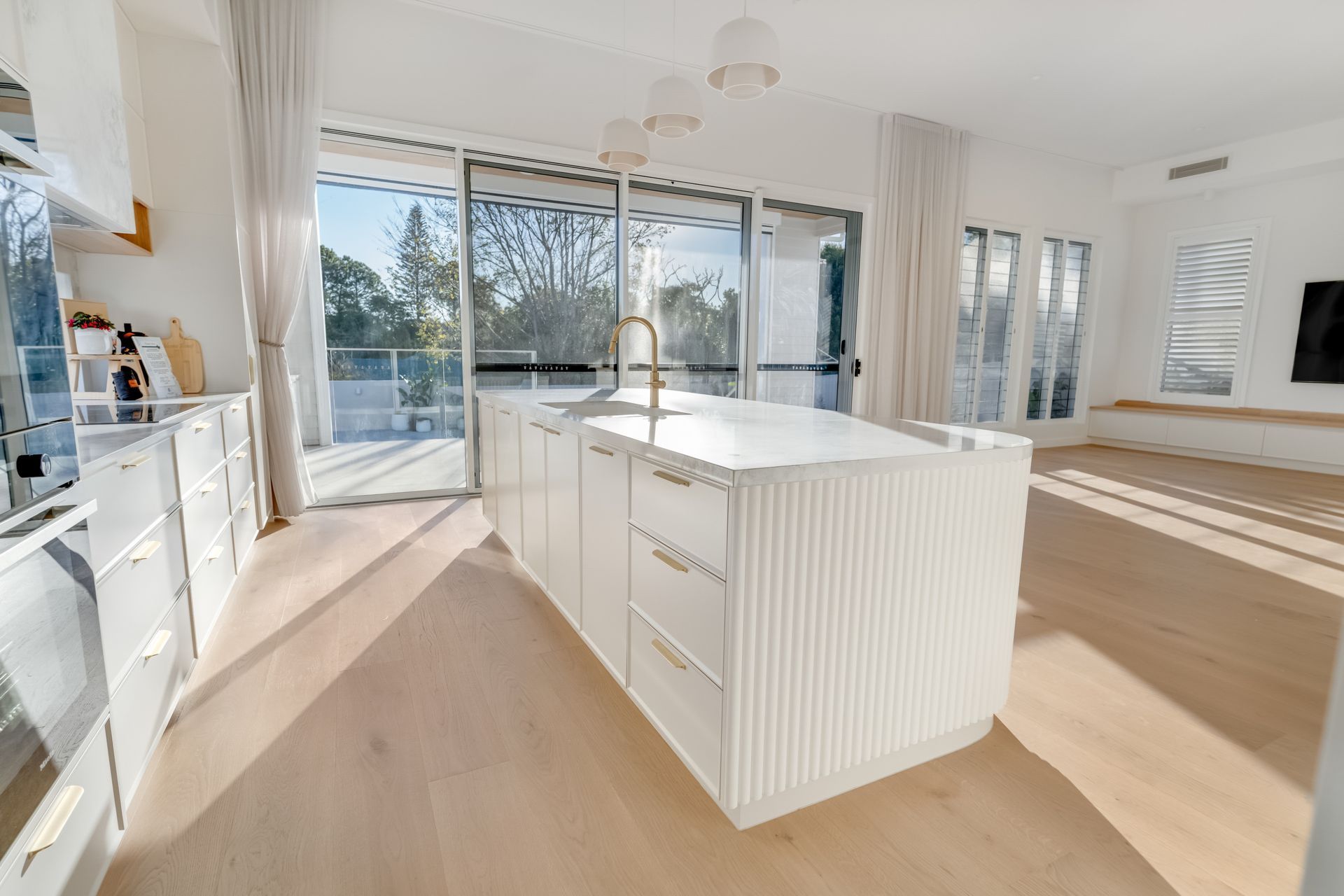 A fluted island and brass tapware anchor the kitchen, glass doors opening straight onto the balcony.