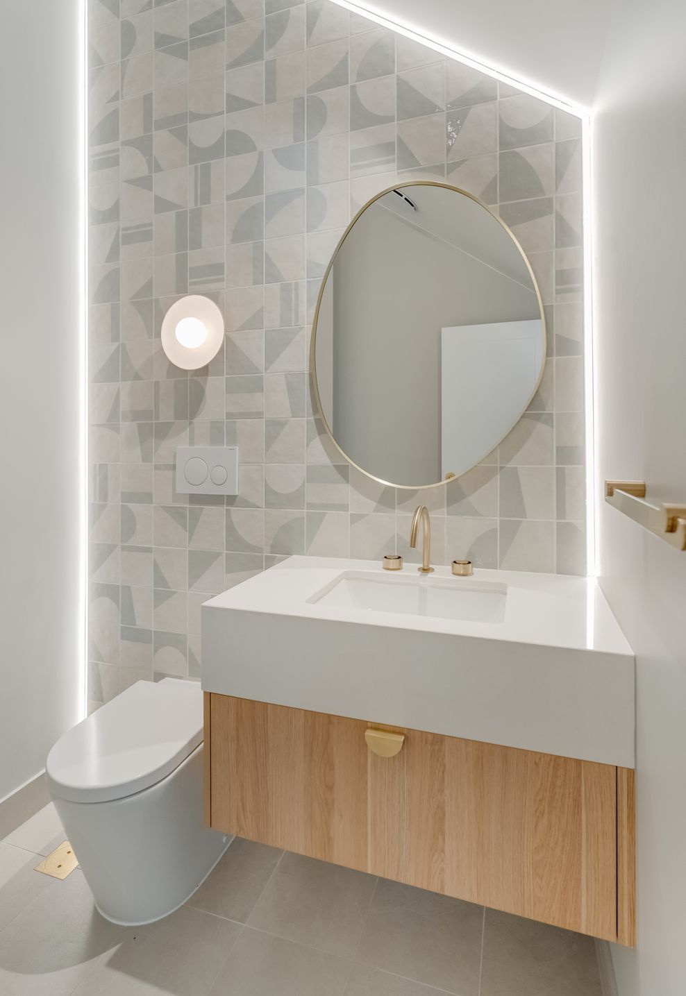 Backlit tiling and a brass-framed mirror give the powder room its quiet glow.