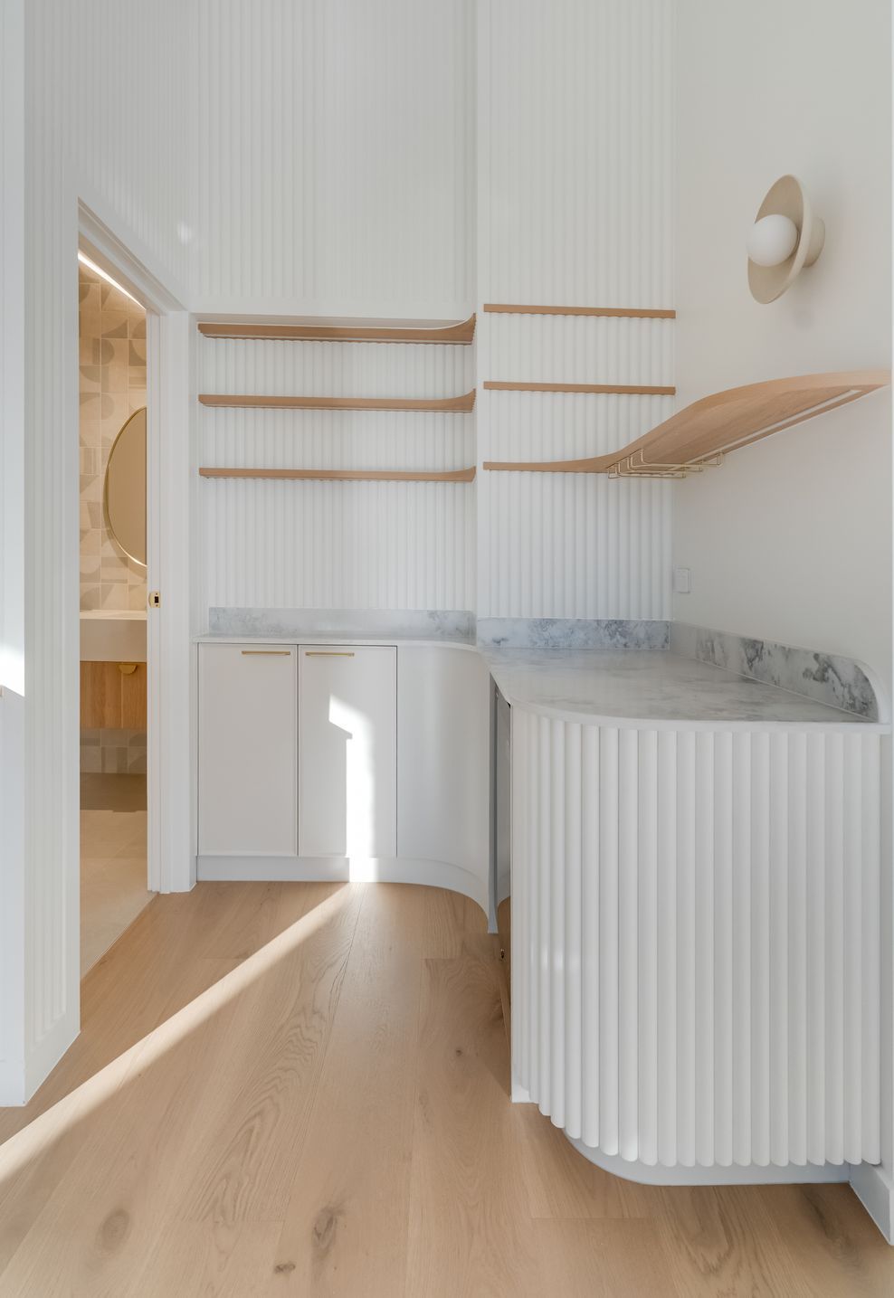 Fluted curved joinery and marble carry the kitchen's detailing into the butler's pantry.