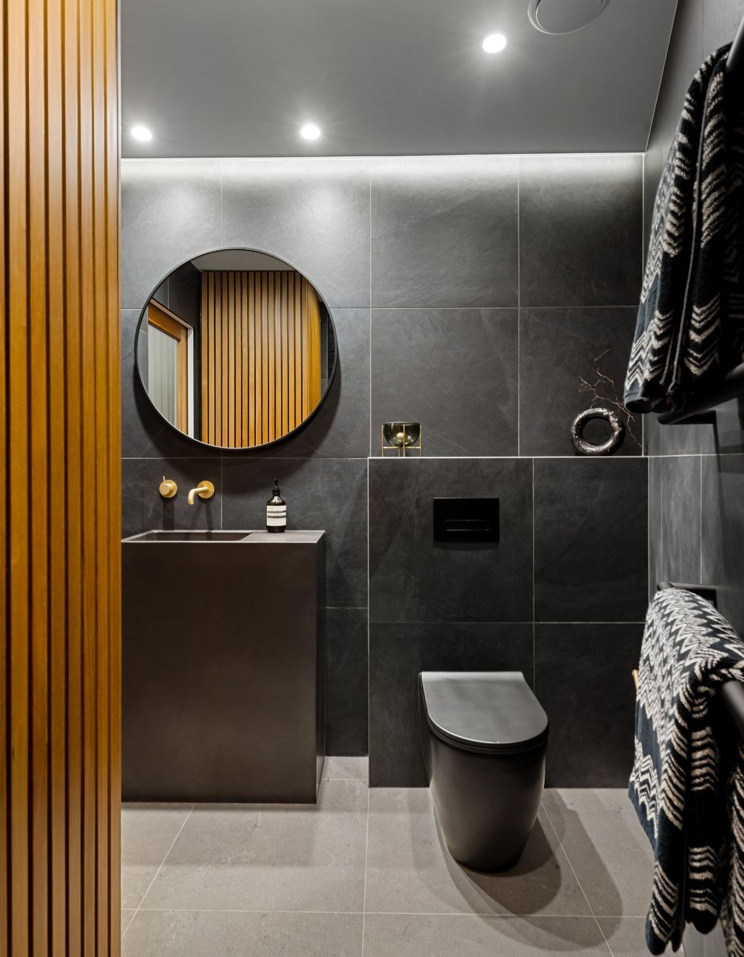 The cupboard features elegant Rimu wood slatted paneling that seamlessly conceals a practical laundry space and additional storage area, combining functionality with aesthetic appeal.