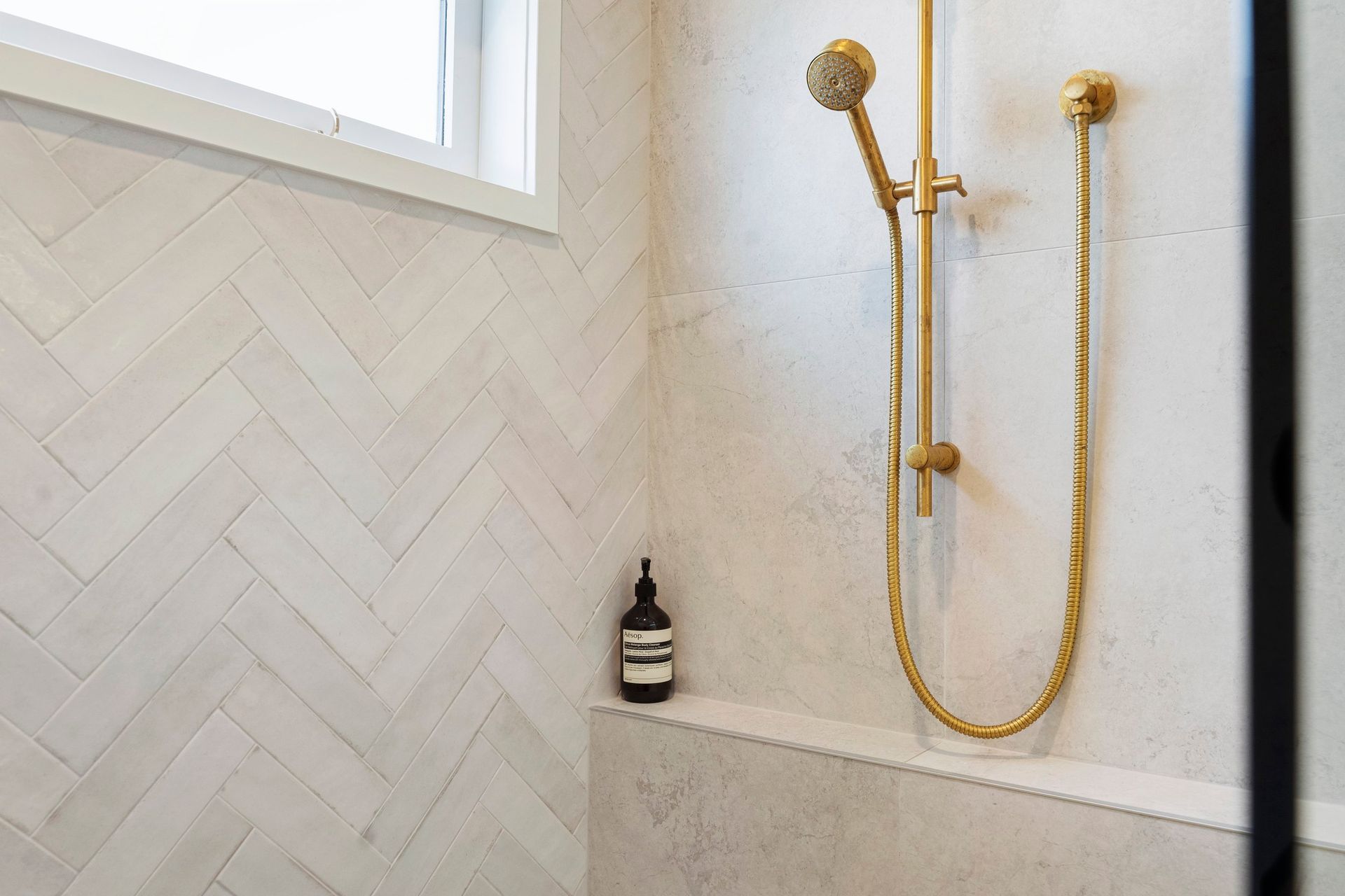 The Tribeca Gypsum white herringbone tiles on the back wall introduce a beautiful texture and understated visual interest to the space, setting the perfect stage for the Progetto organic brushed brass shower head to stand out. The elegant pattern of the tiles enhances the overall aesthetic, creating a soft, contemporary backdrop that beautifully contrasts with the warm tones of the brass fixture. This thoughtful design choice not only elevates the shower area but also adds a touch of sophistication, making it a stunning focal point in the bathroom.